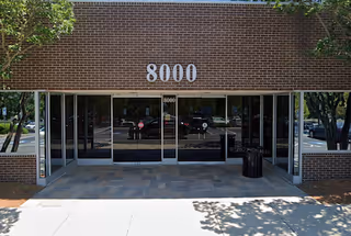 Brick exterior of a building with glass doors and the number 8000 above