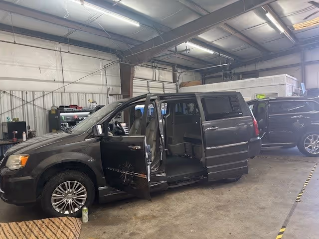 Gray mobility van with open doors inside a large workshop, surrounded by tools and other vehicles.