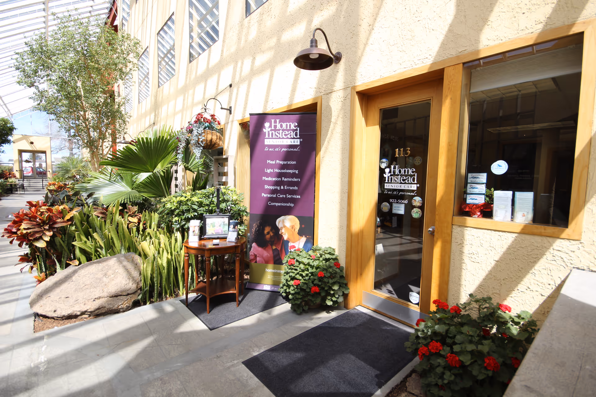 Exterior entrance of Home Instead with wooden door, plants, and a purple banner.