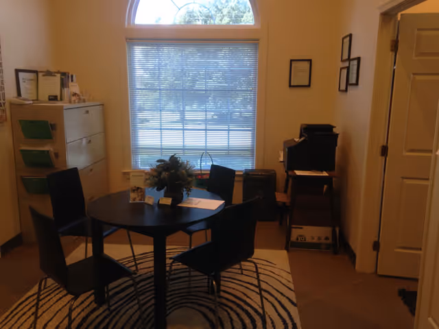 Round table and four chairs in a small, well-lit senior living common room.