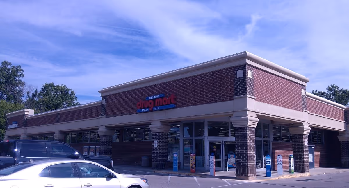 Brick storefront with Discount Drug Mart signage, large windows, parked cars, and blue sky.