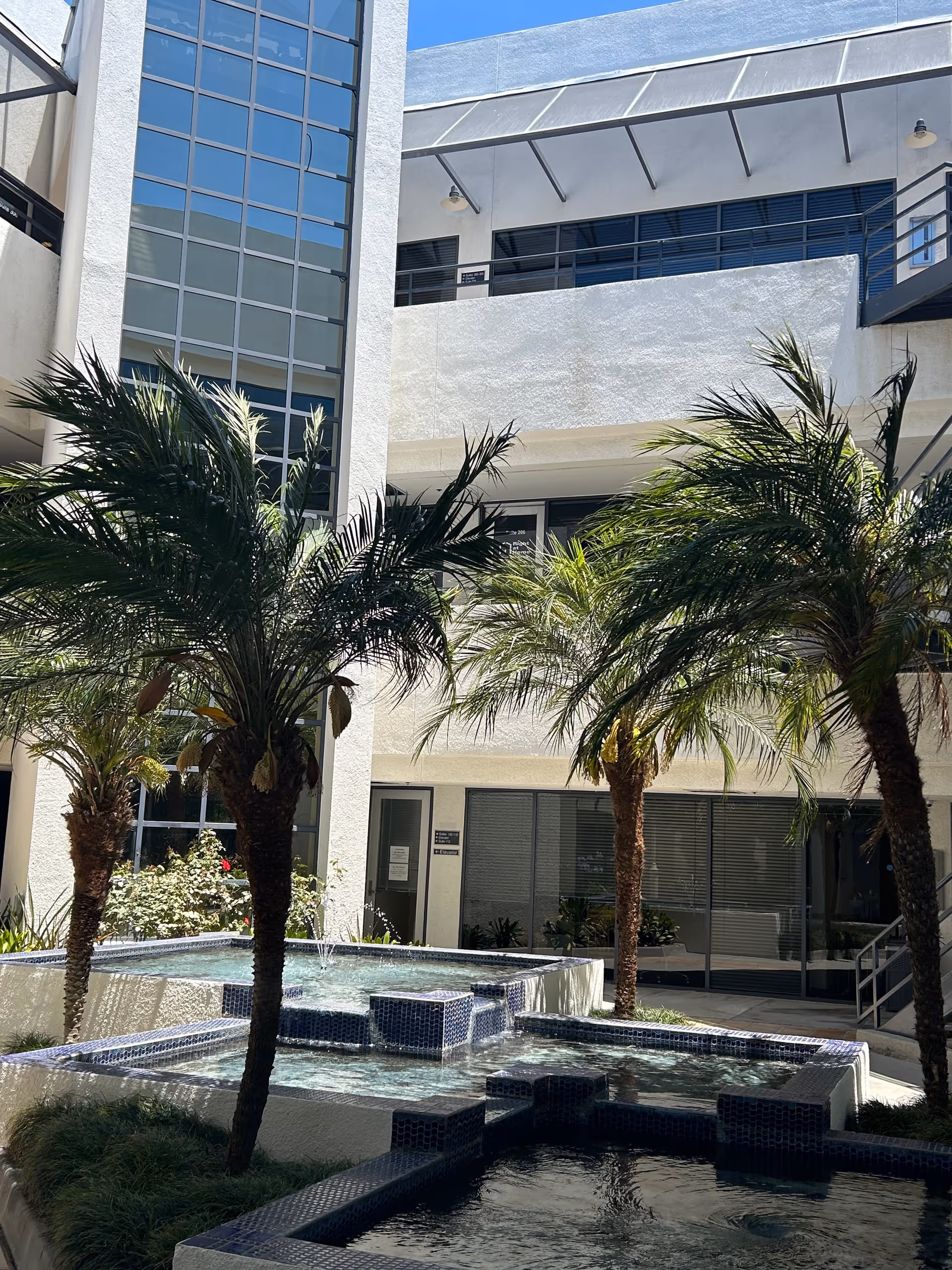 Exterior view of a senior living courtyard with a tiered fountain and palm trees.