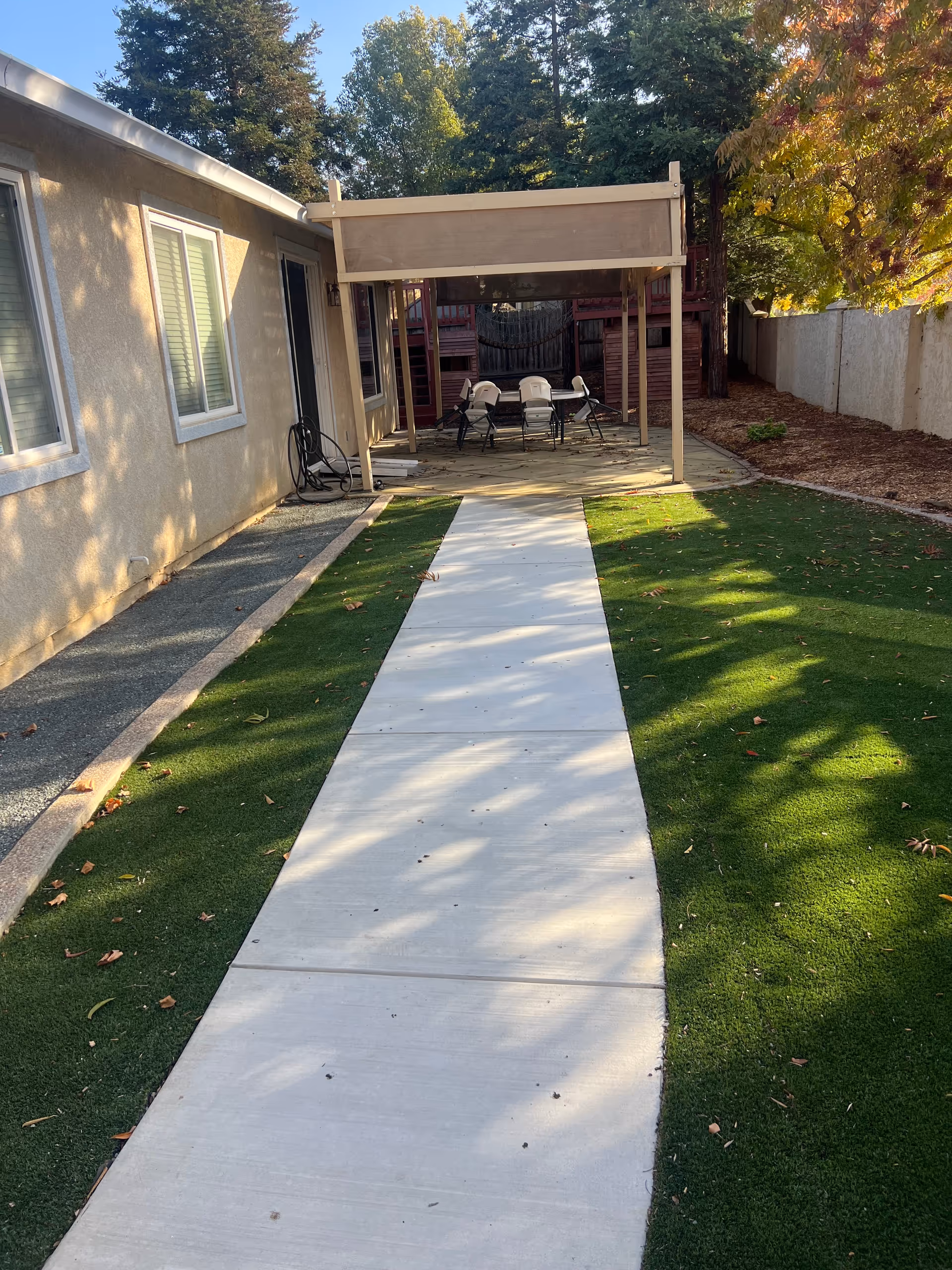 Outdoor backyard patio with a covered seating area, concrete pathway, and surrounding lawn.