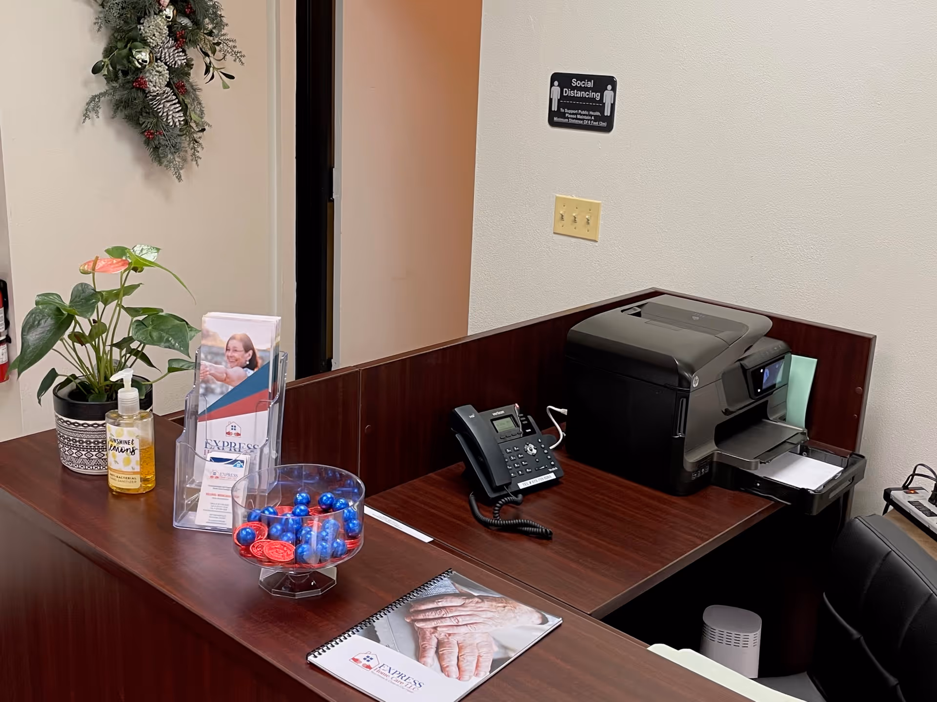 Office front desk with printer, phone, plants, brochures, sanitizer, and candy bowl.