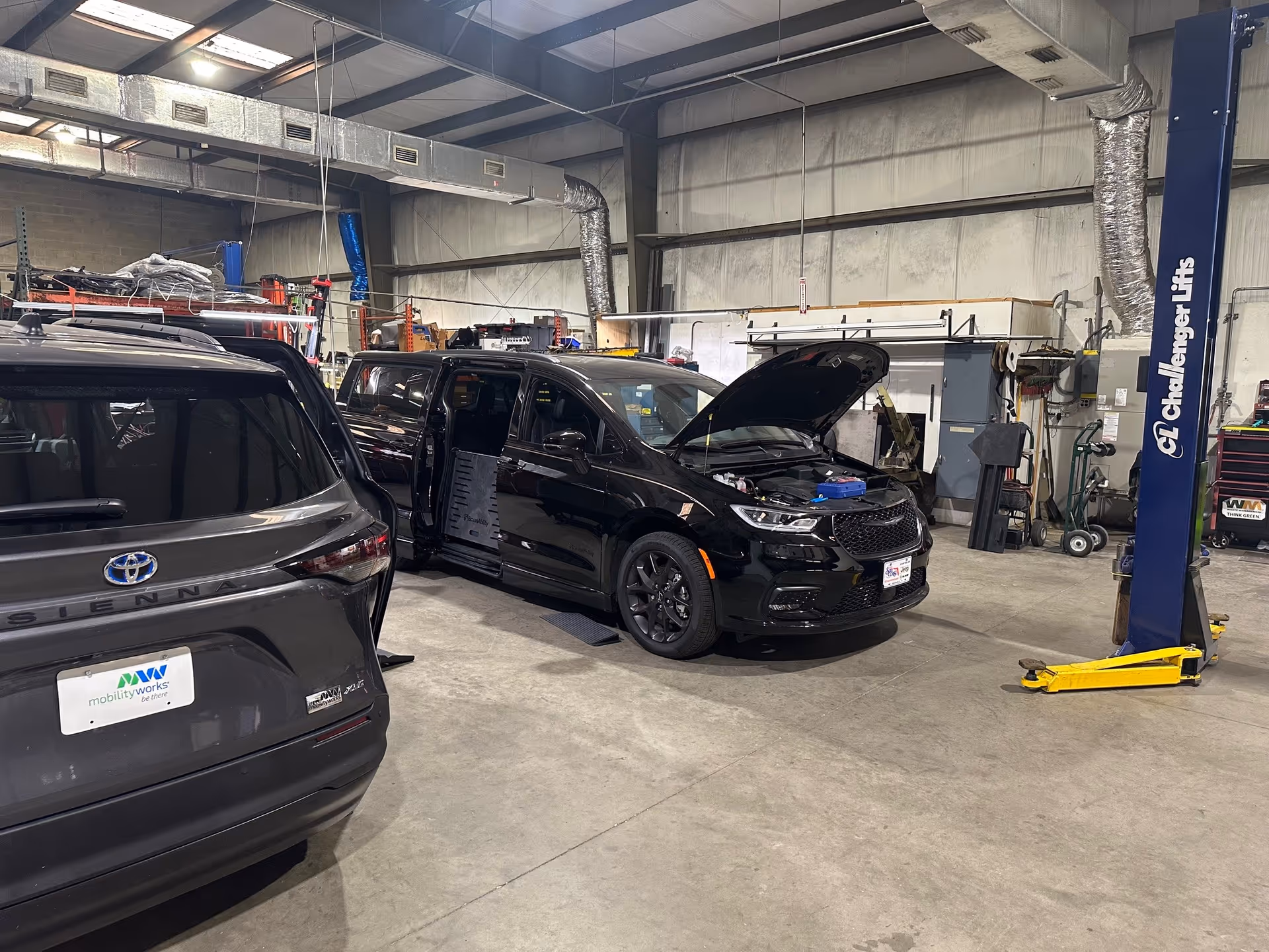 Indoor MobilityWorks service shop showing cars, equipment, and raised hoods.