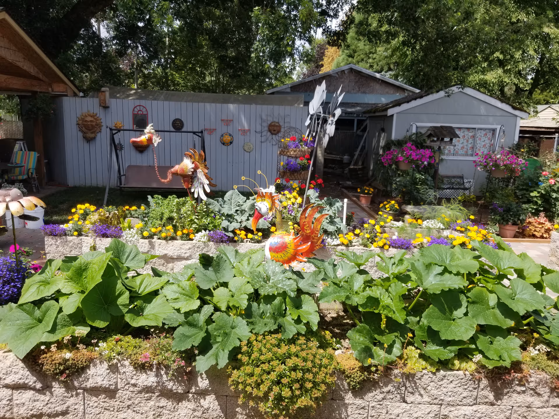 Colorful garden beds, flowers, and decorative sculptures in a sunny outdoor yard.