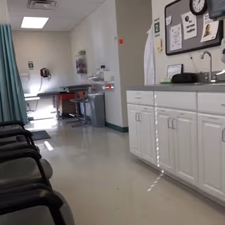 A clinical hallway with seating, a sink station, and white cabinetry.