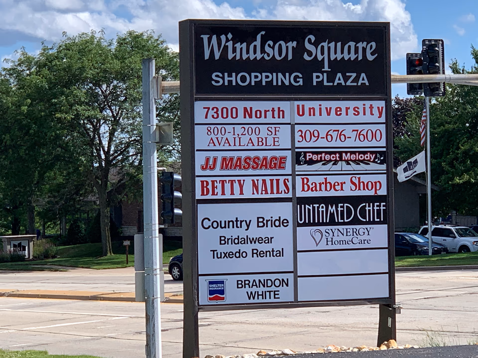 Tall multi-panel exterior signboard advertising Windsor Square Shopping Plaza tenants in a parking lot.