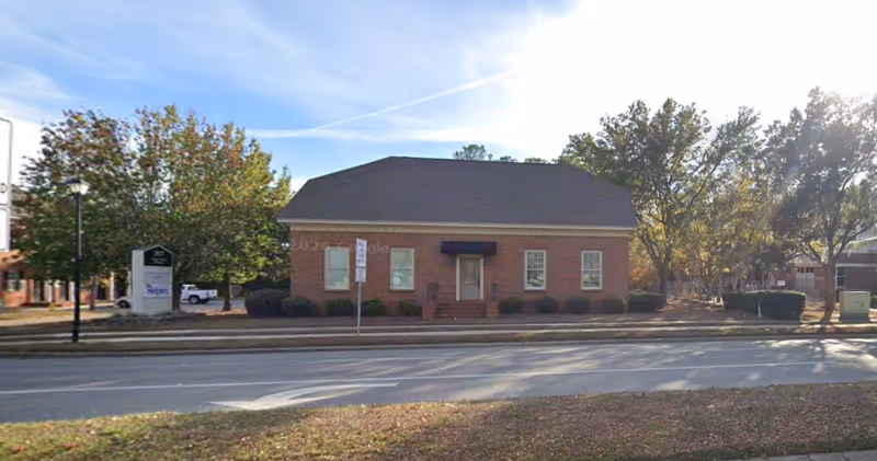 Brick building labeled Senior Helpers on a street, with trees and a sidewalk.
