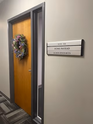 Wooden door with a wreath in a hallway beside a sign reading Home Instead HR