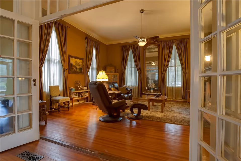 Elegant living room with wood floors, recliner, coffee table, and heavy drapes over windows.
