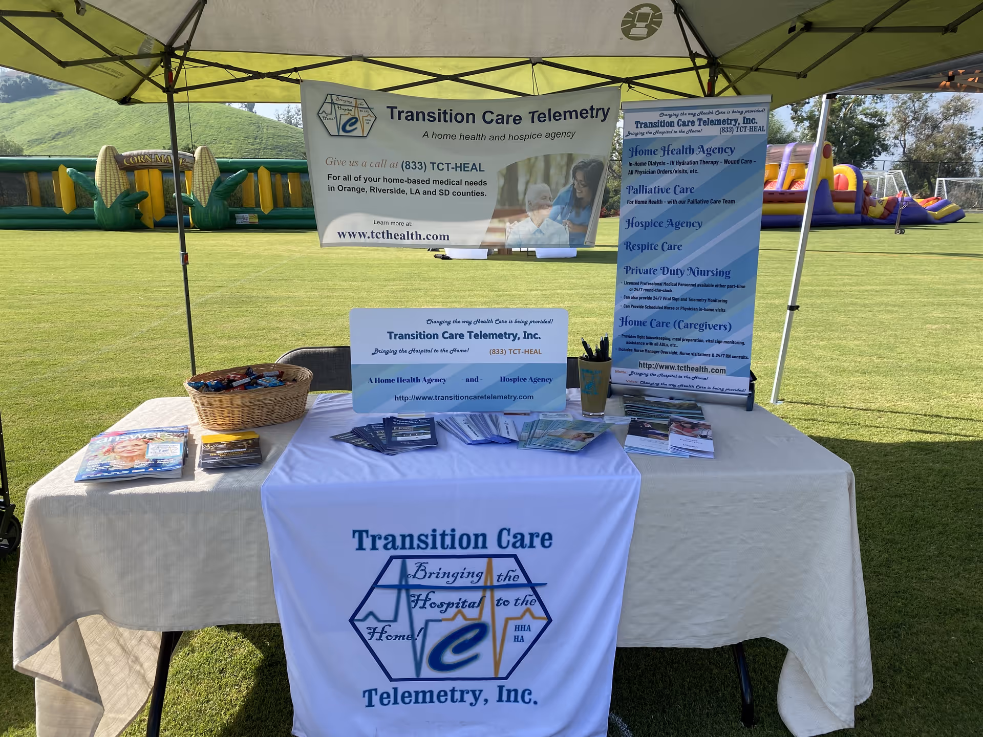 Outdoor health fair booth under a tent promoting Transition Care Telemetry with banners.