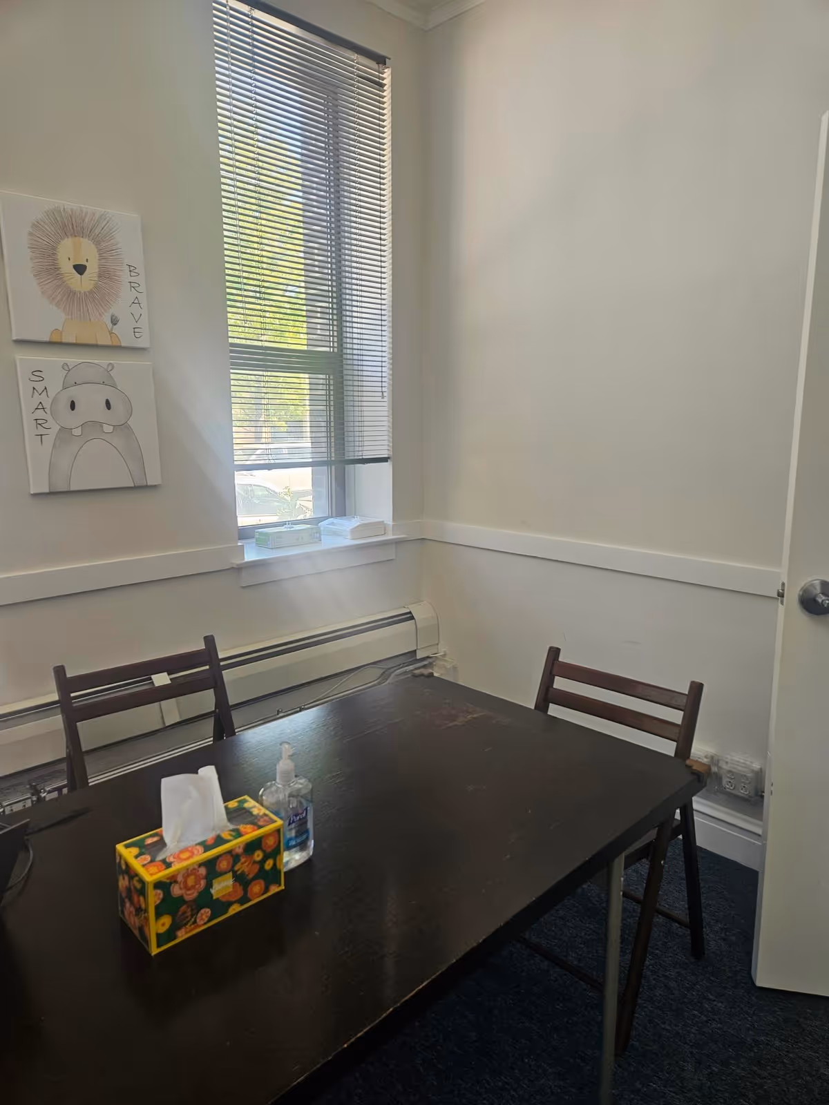 Small interior dining area with dark table, two chairs, and window blinds.
