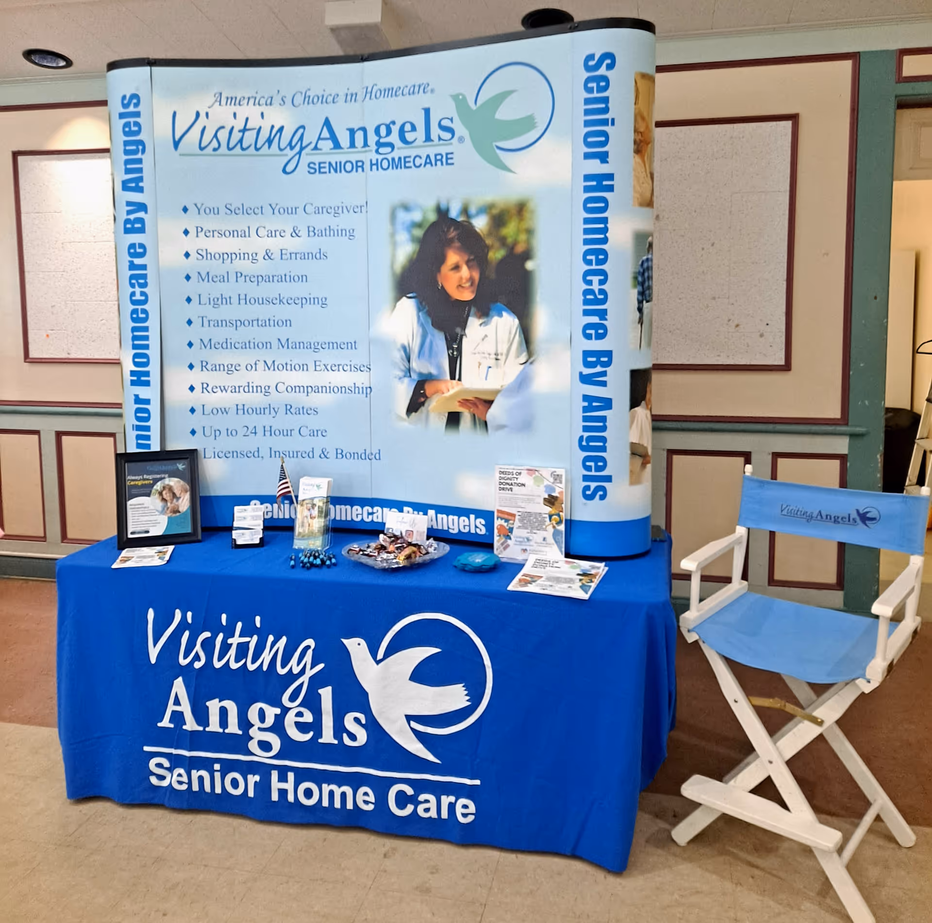 Promotional booth for Visiting Angels Senior Homecare with banner, blue tablecloth, and chair.