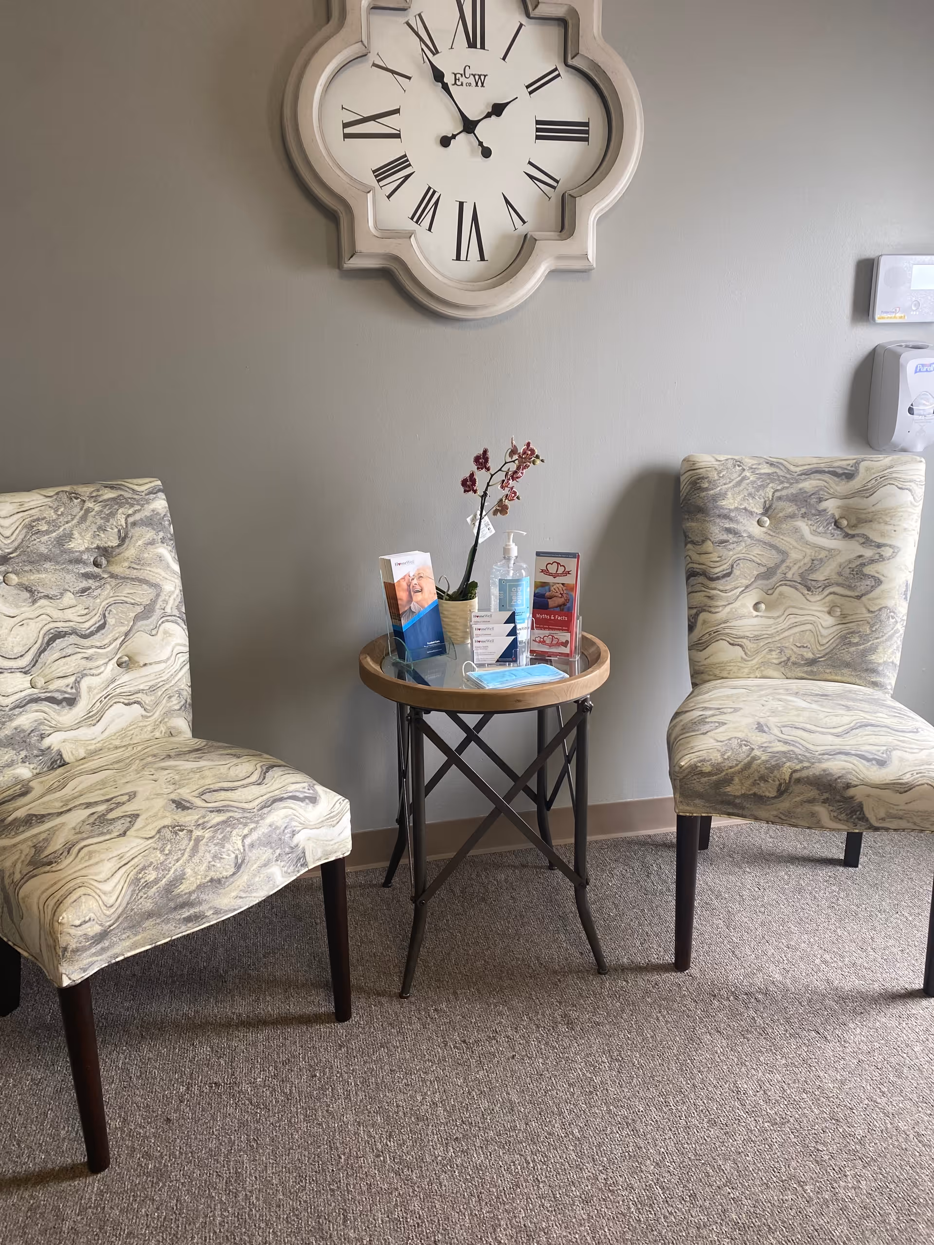 Two patterned chairs flank a small round table with brochures in a waiting area.
