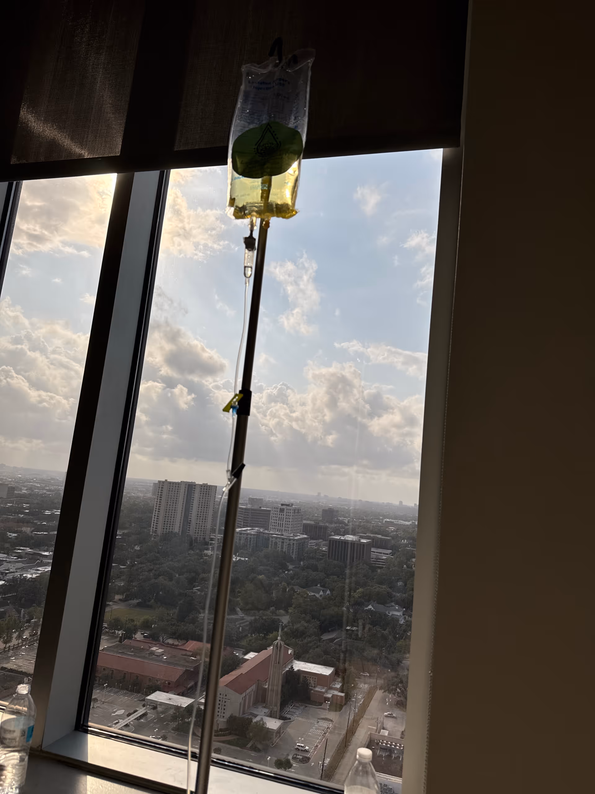 IV bag on stand by window, overlooking a city from a high-rise room.