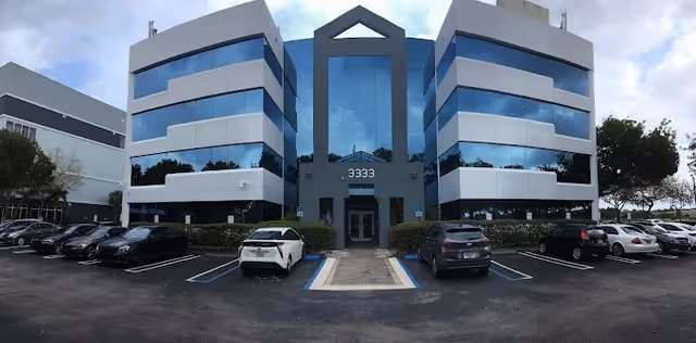 Symmetrical modern building with blue-tinted glass and a front parking lot.