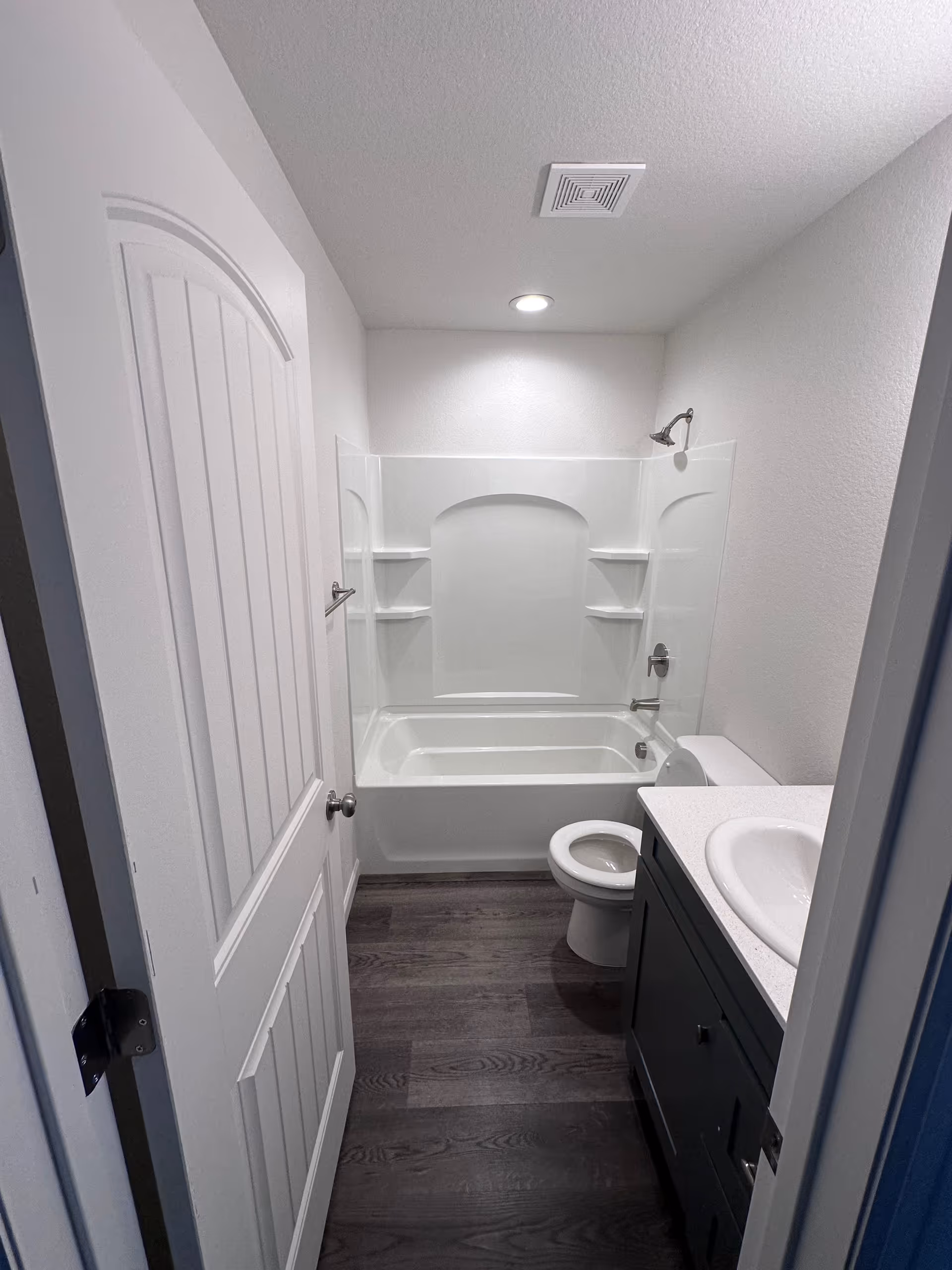 Small bathroom with tub and shower surround, toilet, and vanity in a clean senior facility.