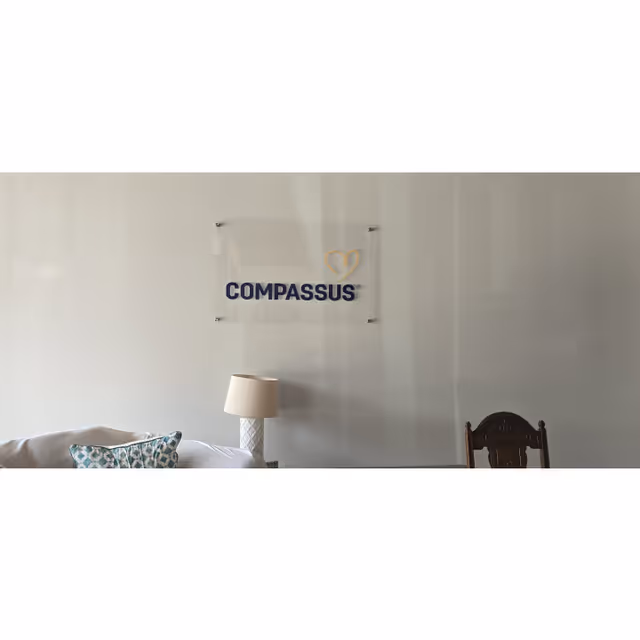 Living room scene with Compassus sign, sofa, lamp, and a wooden carved chair.