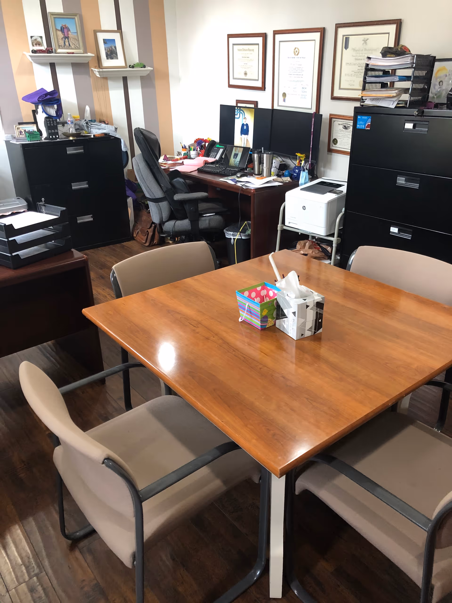 Office workspace with a large wooden table, chairs, and filing cabinets.