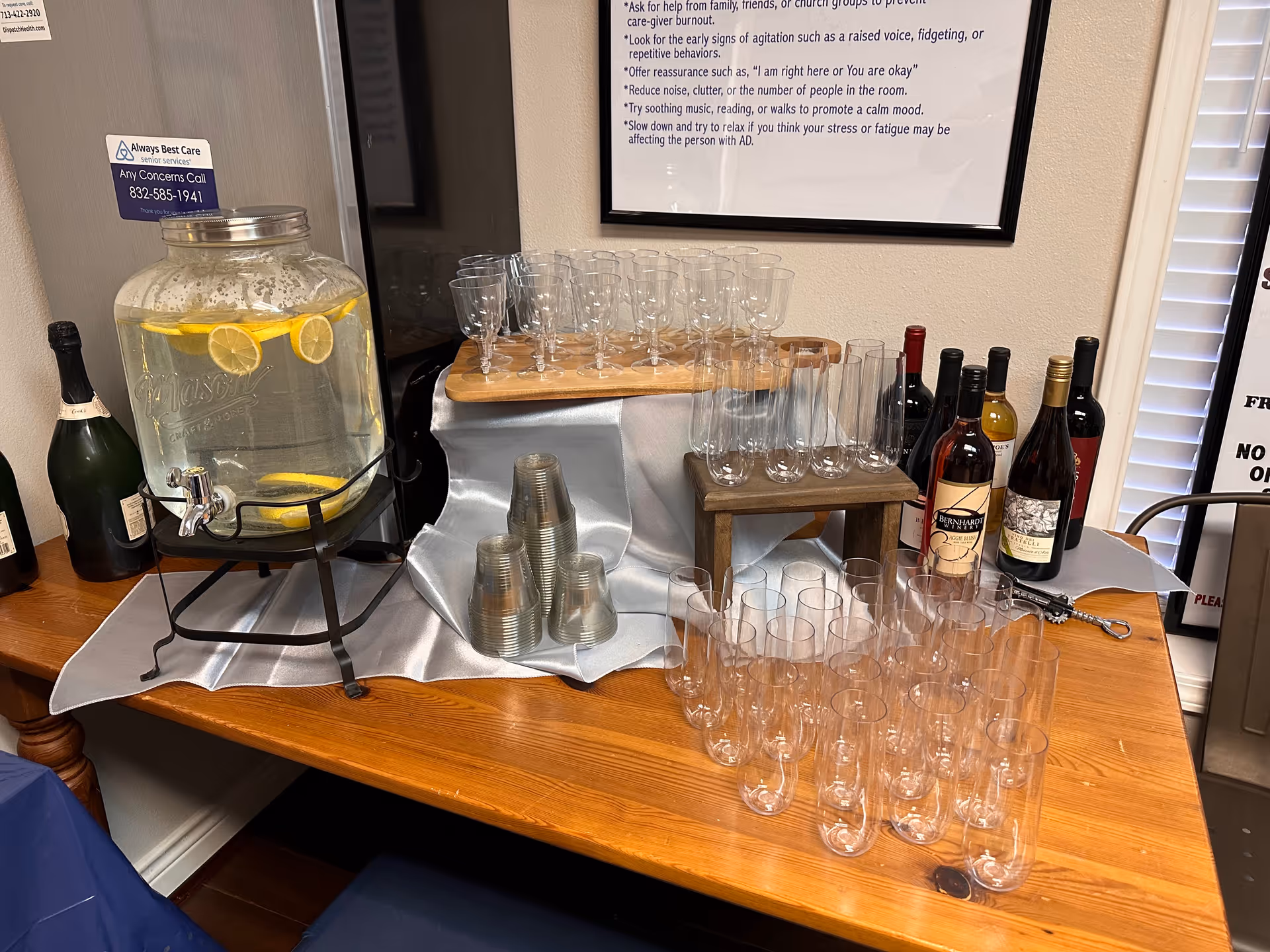Wooden table with glassware, punch dispenser, and wine bottles in an indoor beverage setup.