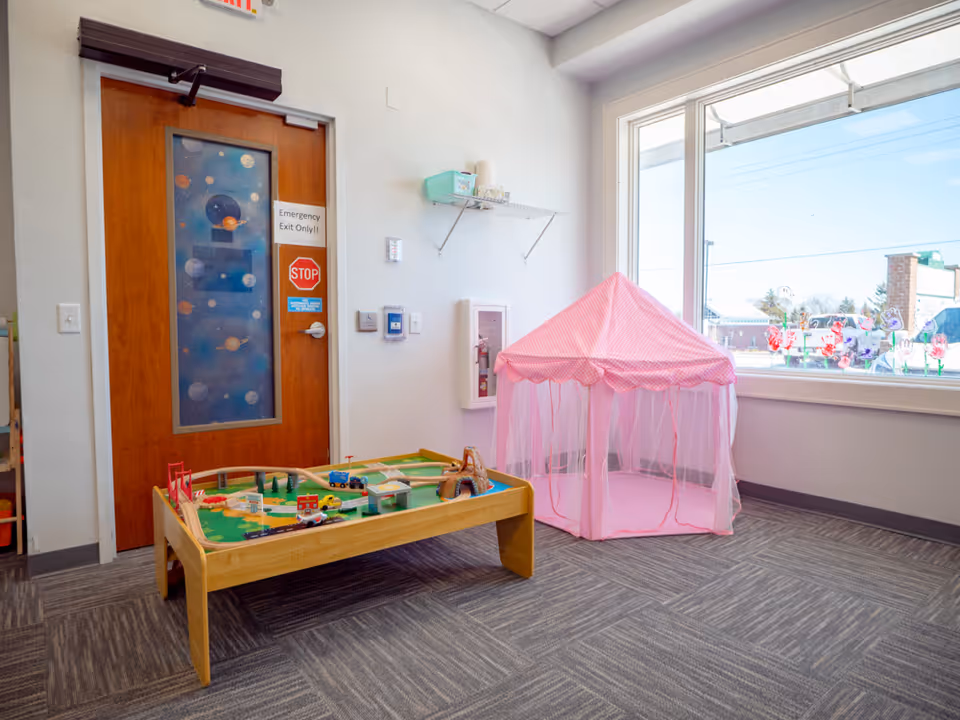 Indoor children's play area with a wooden train table and pink canopy tent in a facility.