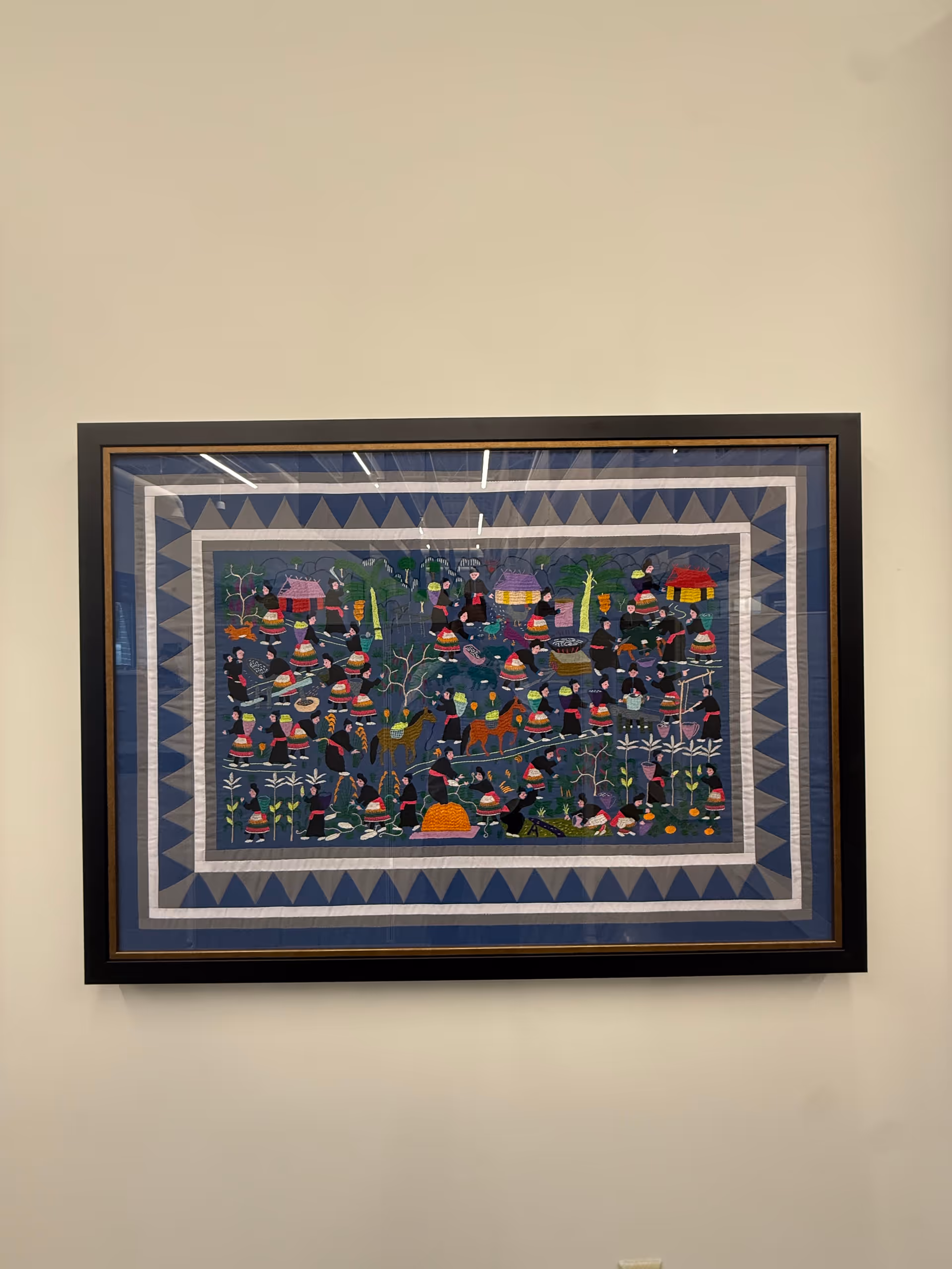 Framed colorful quilt hangs on a light beige interior wall.