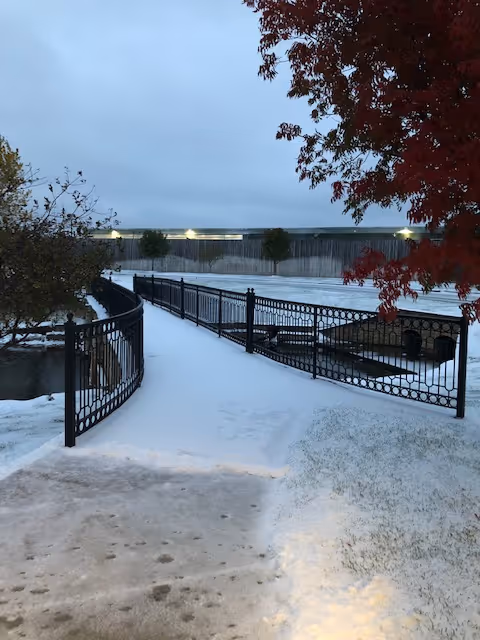 Snowy outdoor path with black iron railing and a fenced courtyard area.