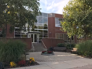Brick building entrance with glass windows, stairs, and landscaped walkway.