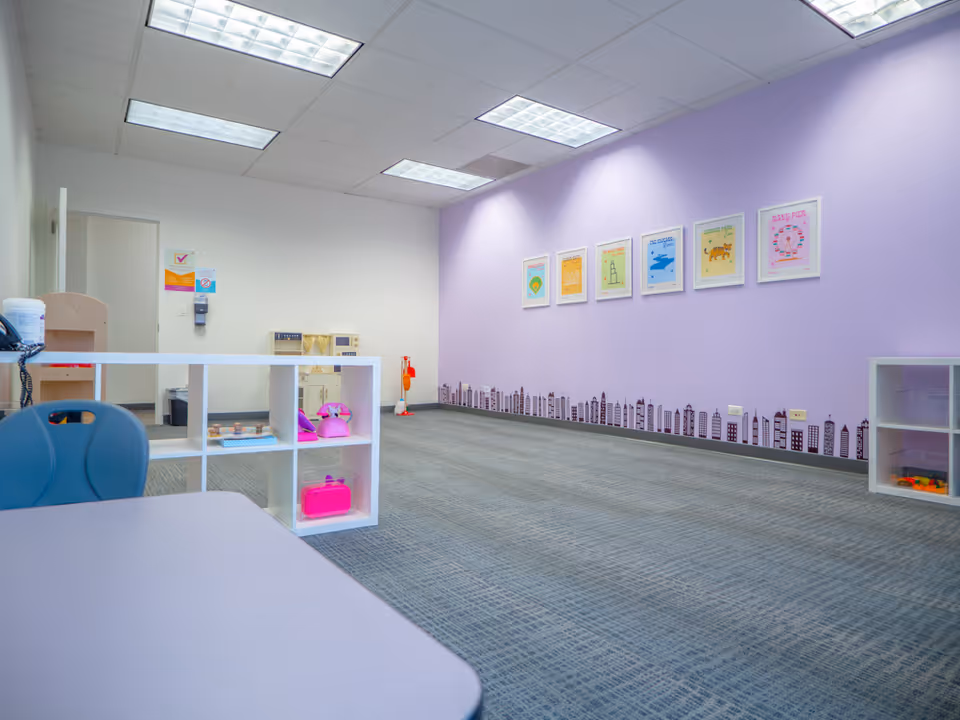 Bright play area inside a facility with a purple wall, framed posters, and toy shelves.