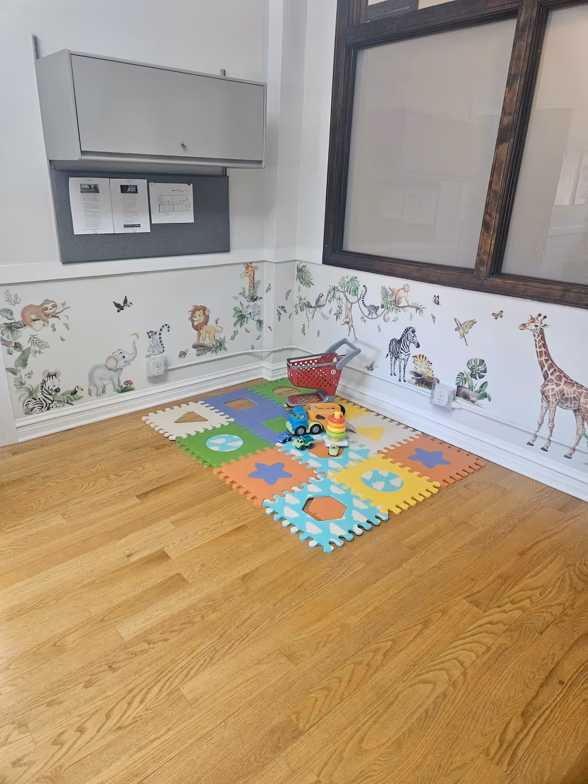 Colorful children's play area with foam mats, toys, and jungle-themed wallpaper in a senior living facility.