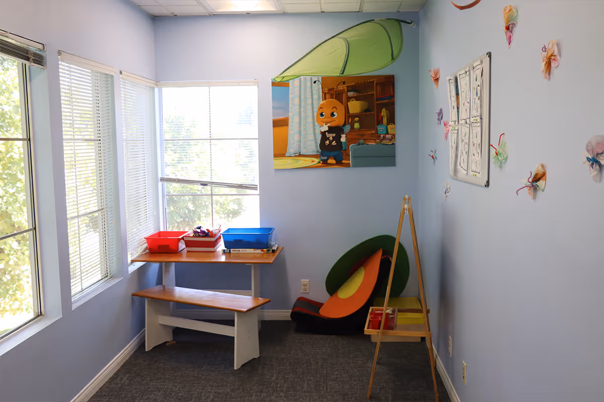 Bright blue playroom corner with a table, bench, toy bins, windows, and wall art.