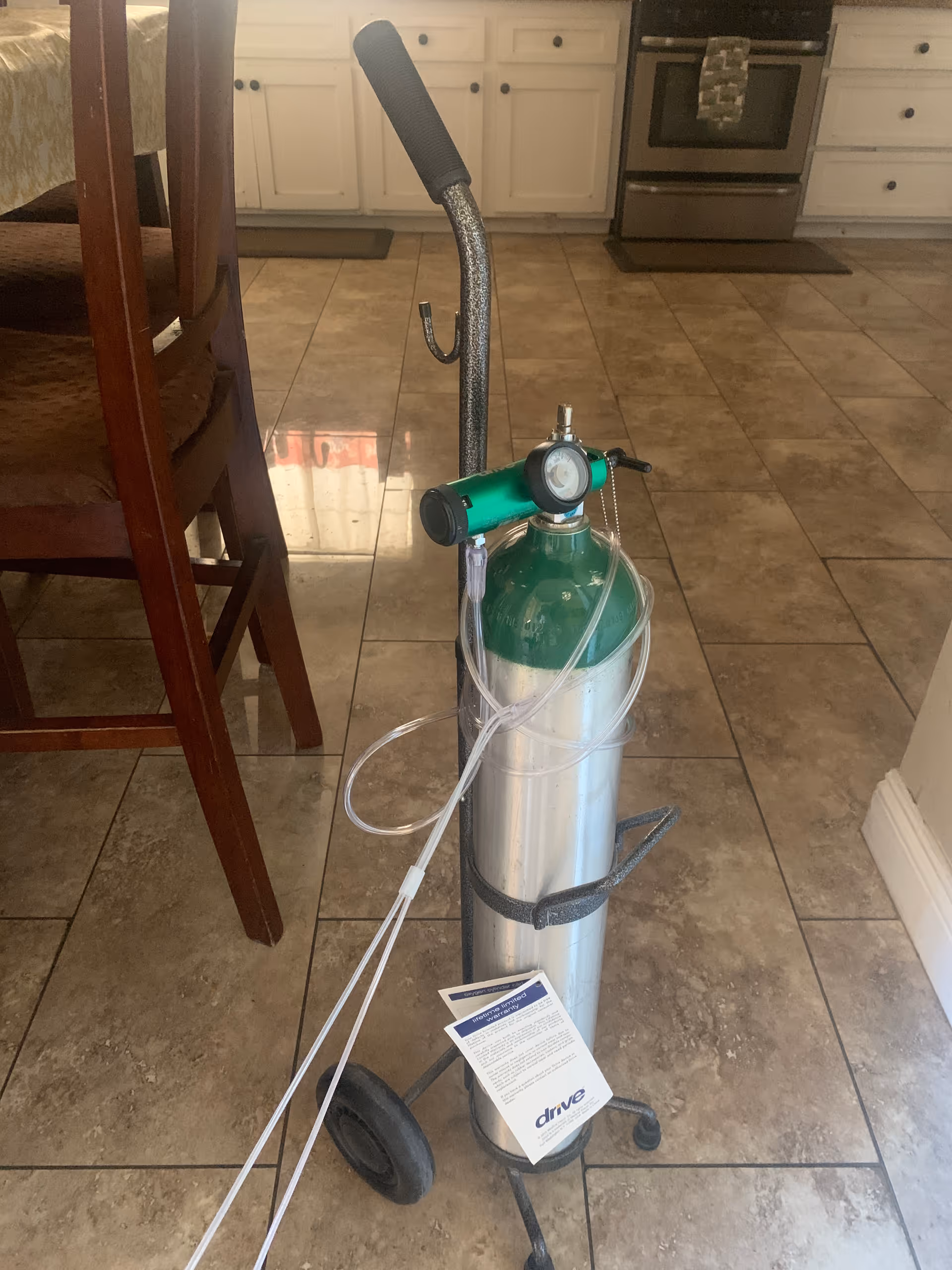 Green oxygen cylinder with regulator and tubing in a kitchen.