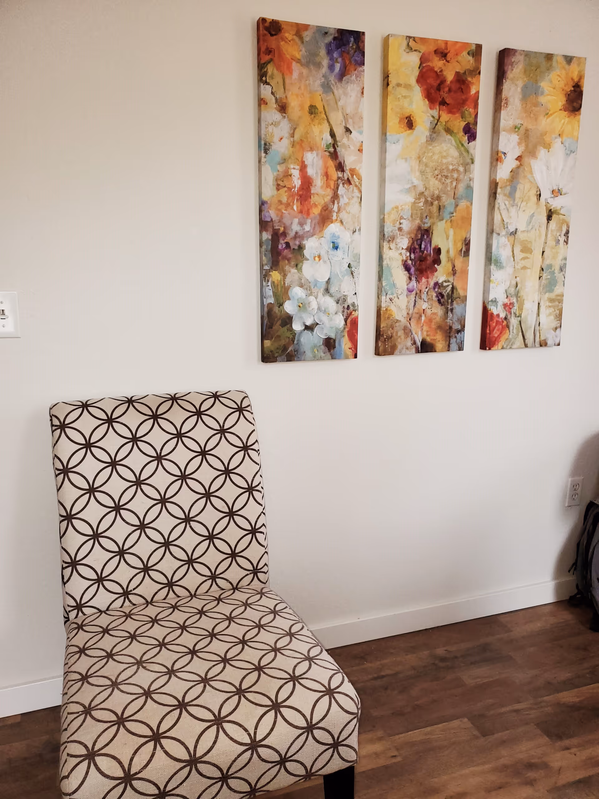 A patterned chair sits beside colorful abstract wall art in a neutral interior.