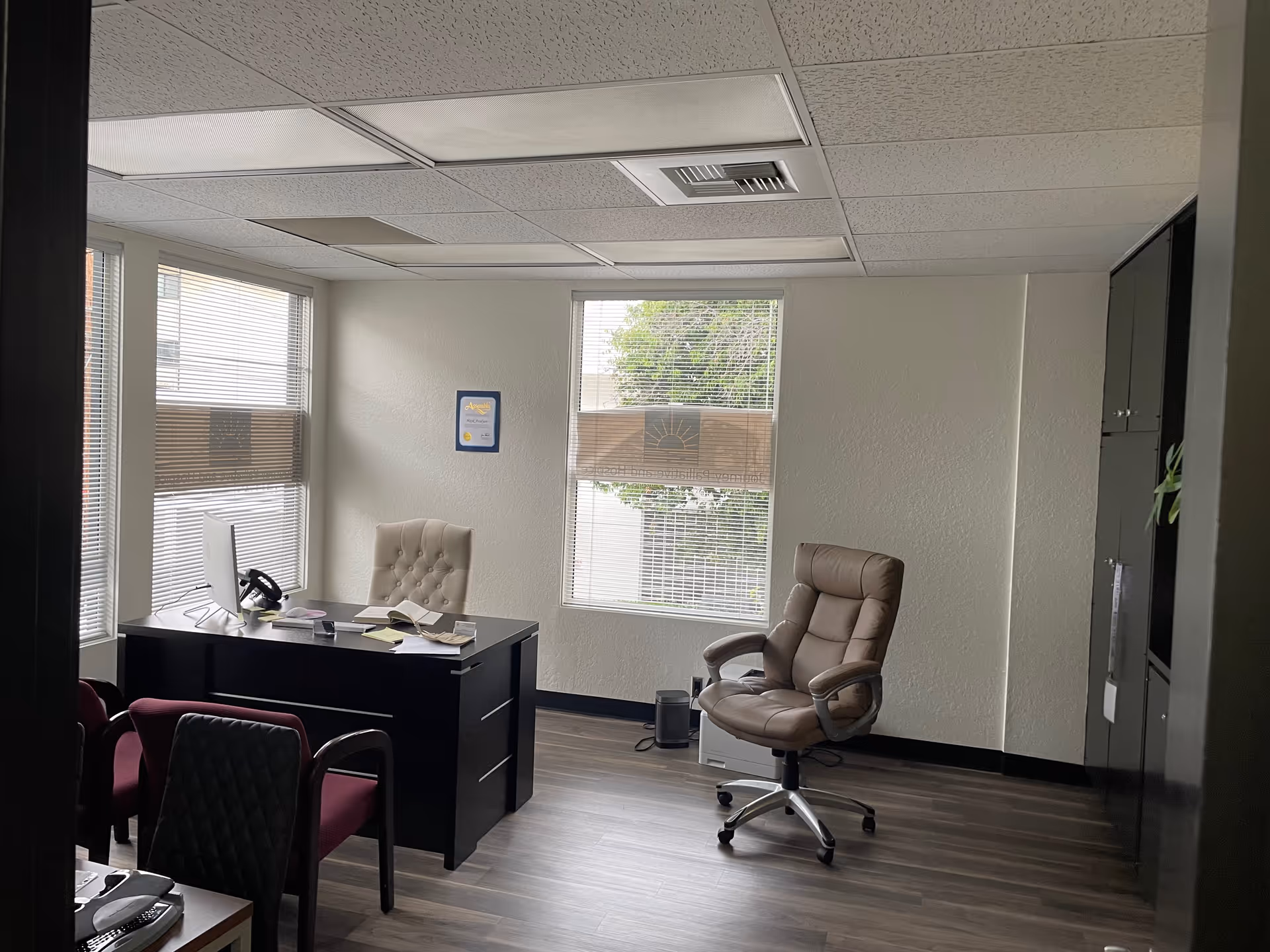 Office workspace inside Journey Palliative and Hospice featuring desk, beige chair, and windows.