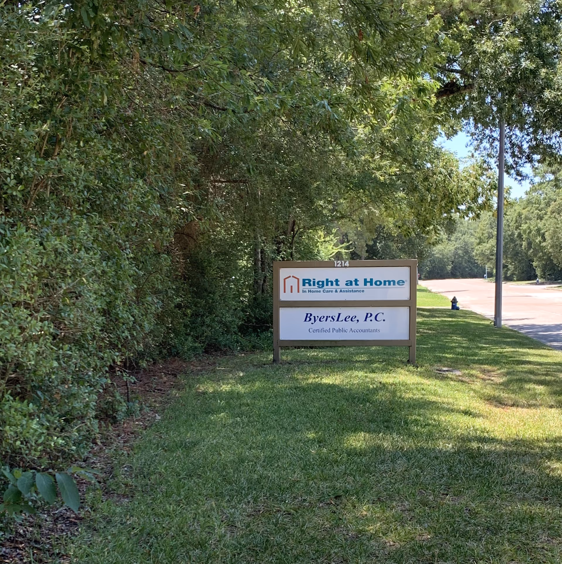 Outdoor sign for Right at Home beside a grassy lawn and leafy trees.