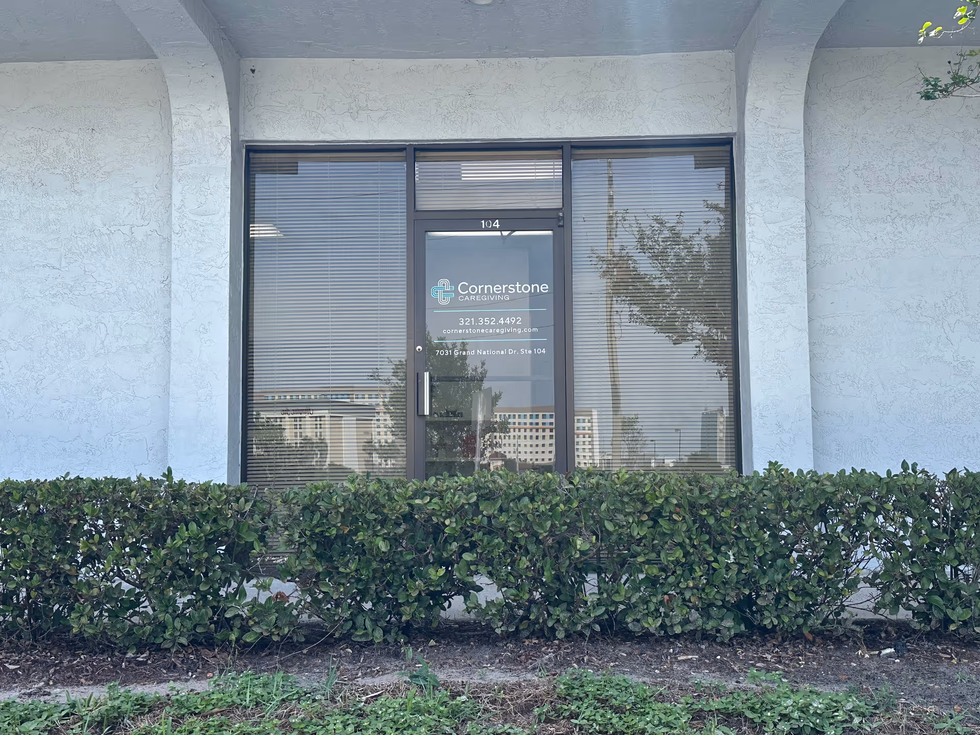 Exterior entry with glass door bearing Cornerstone Caregiving sign and shrubs.
