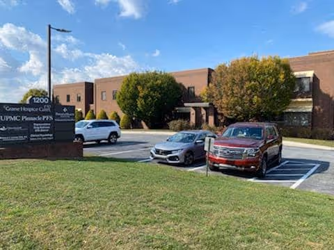 Brick Grane Hospice Care building with parked cars and manicured trees.