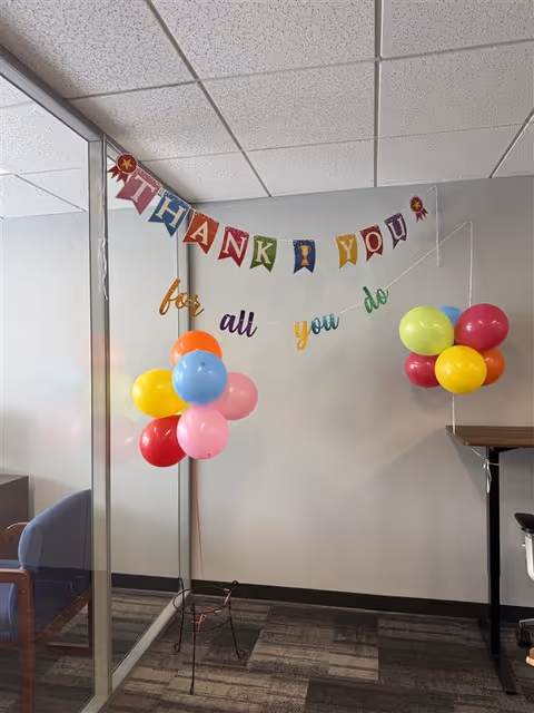 Colorful 'Thank You' banner and balloons decorate a glass-walled interior space.