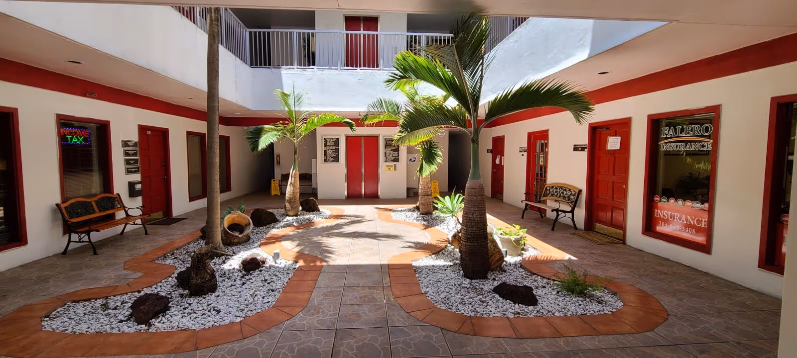 Indoor courtyard at Elite Care At Home with palm trees, benches, red doors, and white rocks.