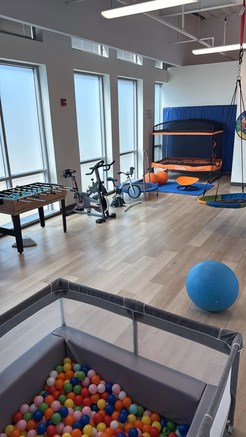 Interior therapy room with exercise bikes, trampoline, swing, and colorful ball pit for residents
