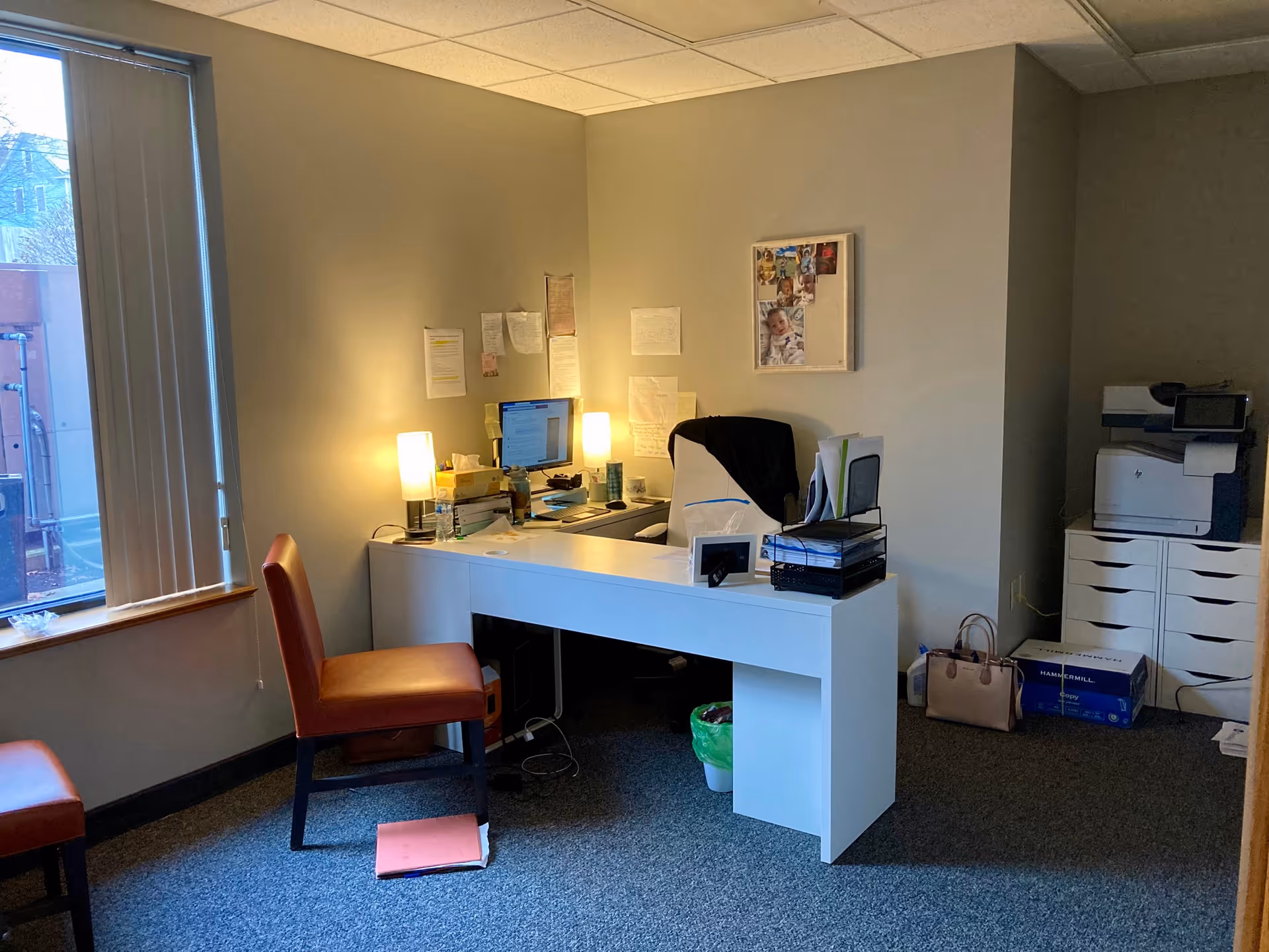 An office workspace inside a senior living facility with a desk, computer, lamp, and printer.