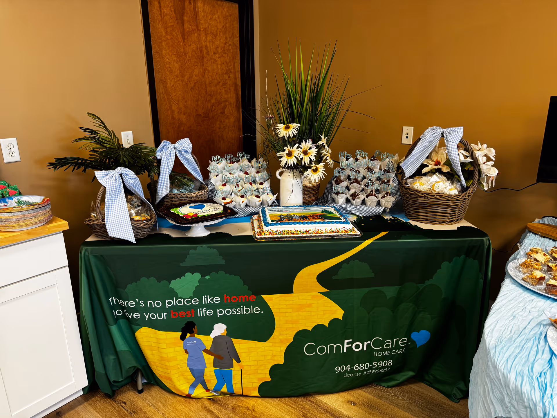 Decorated table with cake, gift baskets, and plants inside a home care facility.