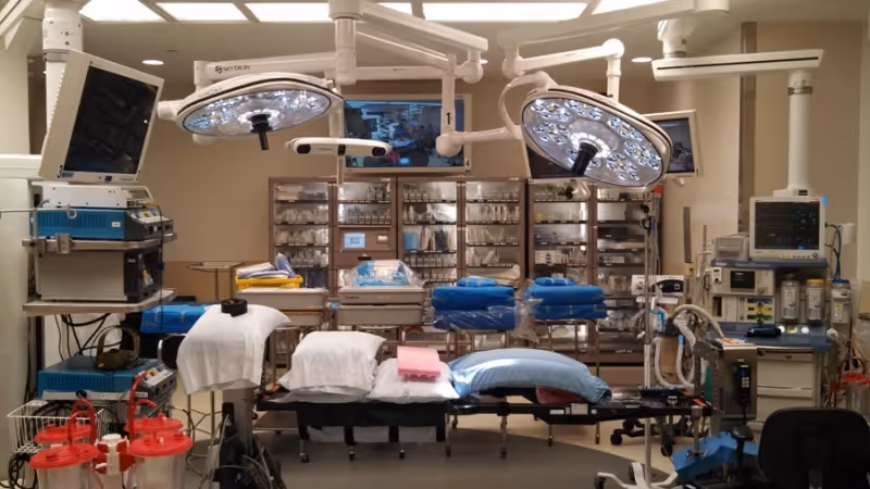 Surgical room with overhead lights, anesthesia equipment, and medical carts.