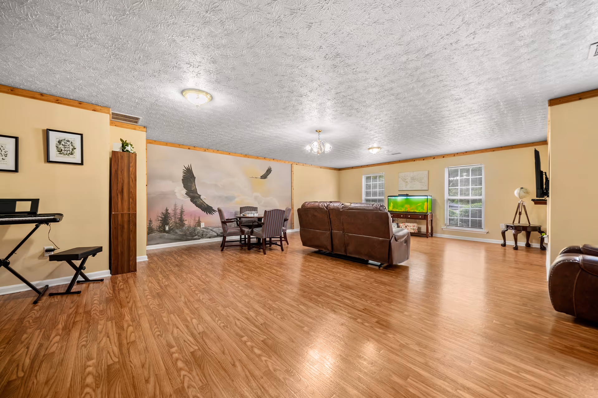 Spacious senior living common area with brown leather sofas, a piano, dining table, and TV