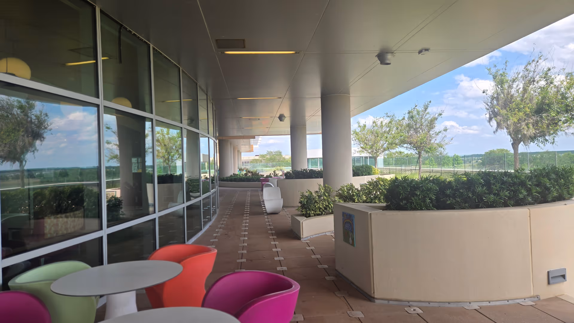 Outdoor seating area along glass-walled building with colorful chairs and planters.