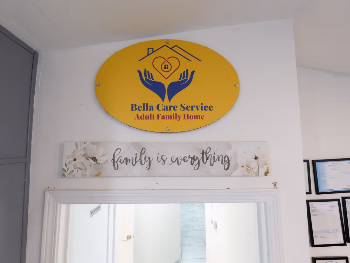 Yellow Bella Care Service sign with 'Adult Family Home' and 'family is everything' plaque in hallway