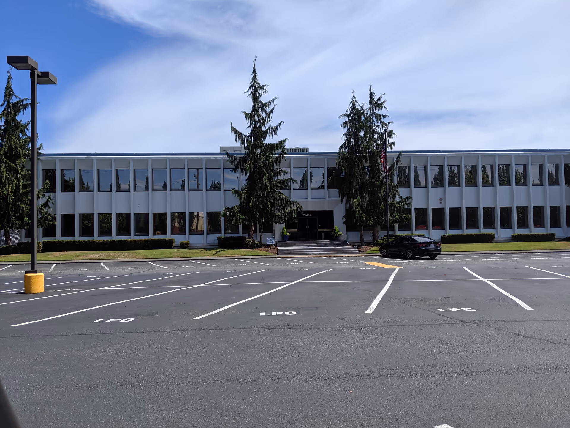 Front exterior of a modern two-story building with a parking lot and trees nearby.