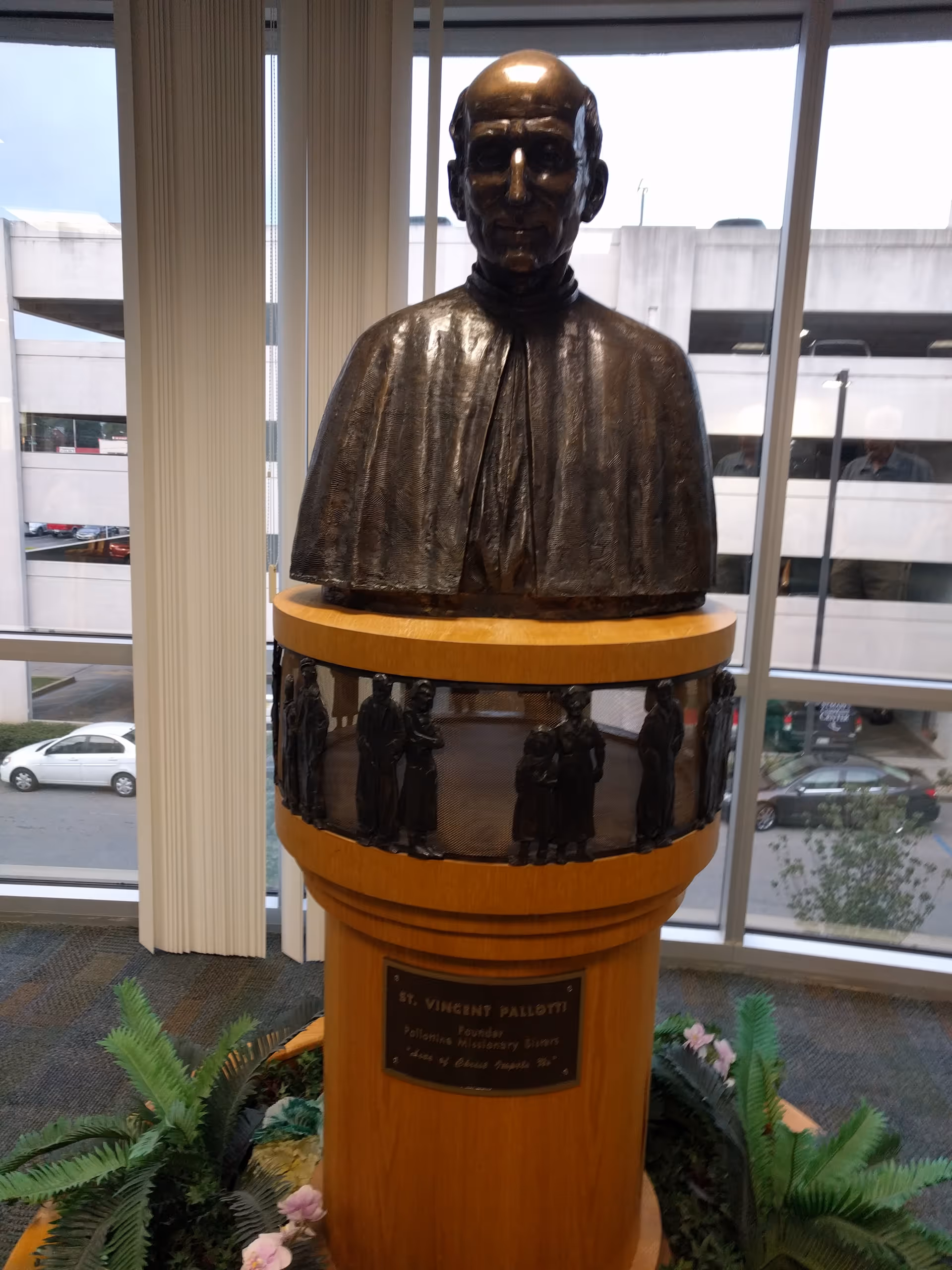 Bronze bust statue on a pedestal inside a windowed lobby.
