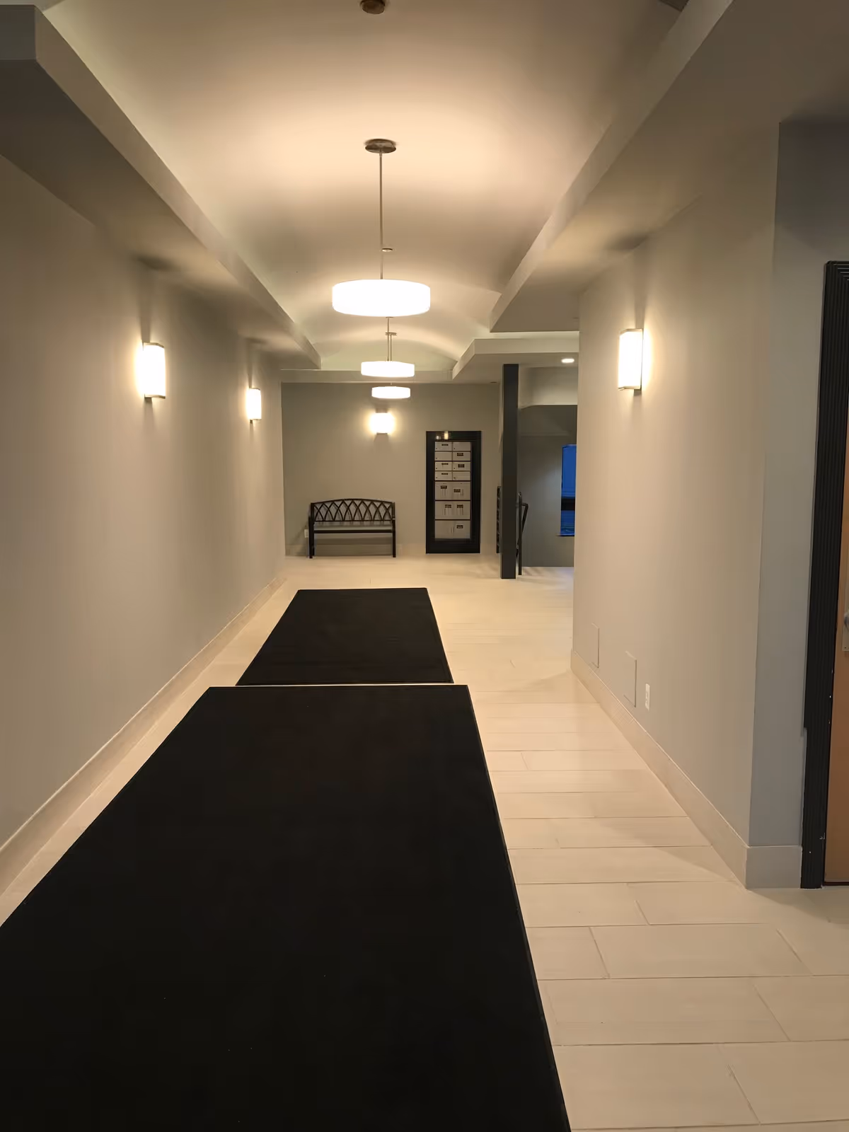 Well-lit hallway with black runners and a bench at the far end.